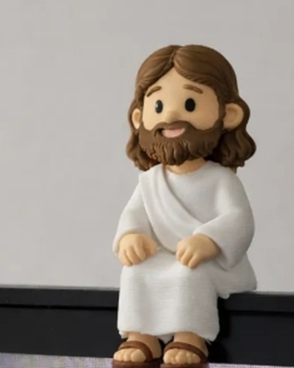 Miniatura de Jesus sentada na borda superior da tela de um notebook, com as pernas para fora.