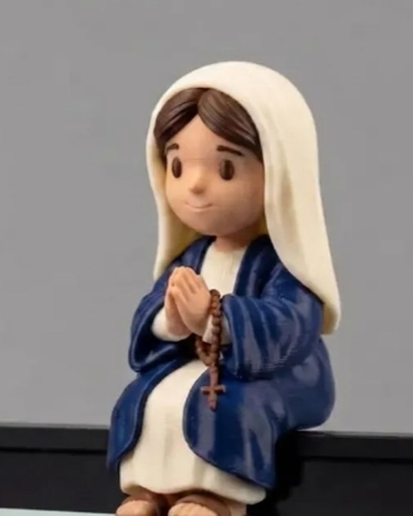 Miniatura de Nossa Senhora sentada na borda de um monitor, com manto azul, véu claro e terço nas mãos.